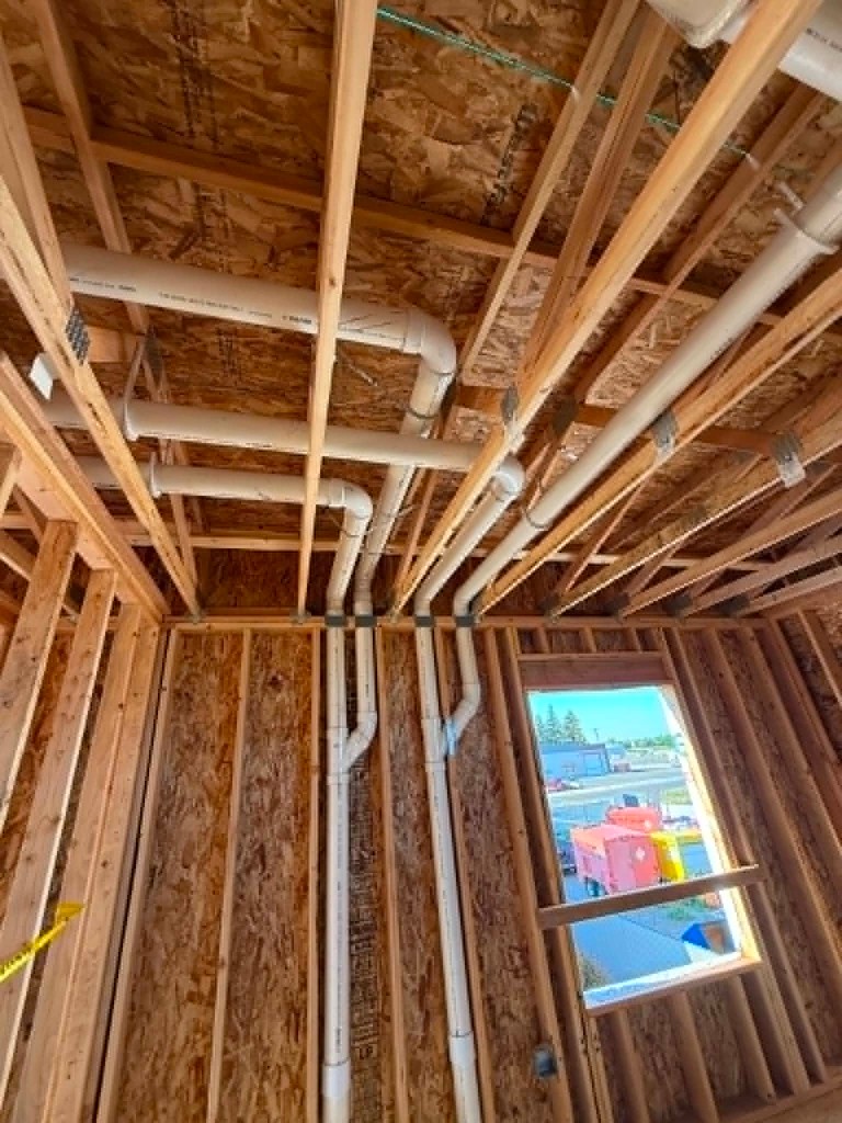 Overhead drain and vent piping routed through framed ceiling joists