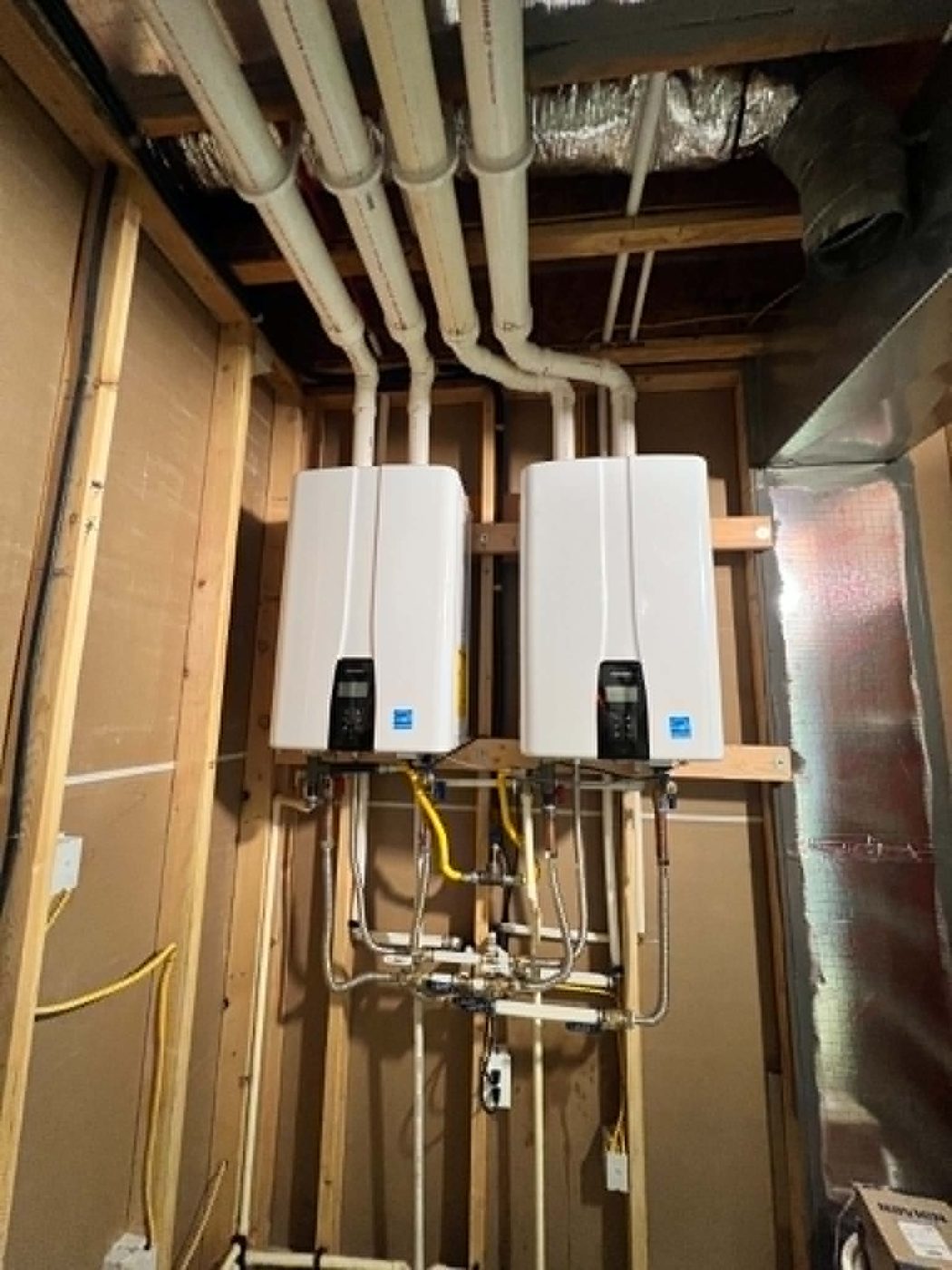 Two tankless water heaters installed on a wall with copper and PEX piping