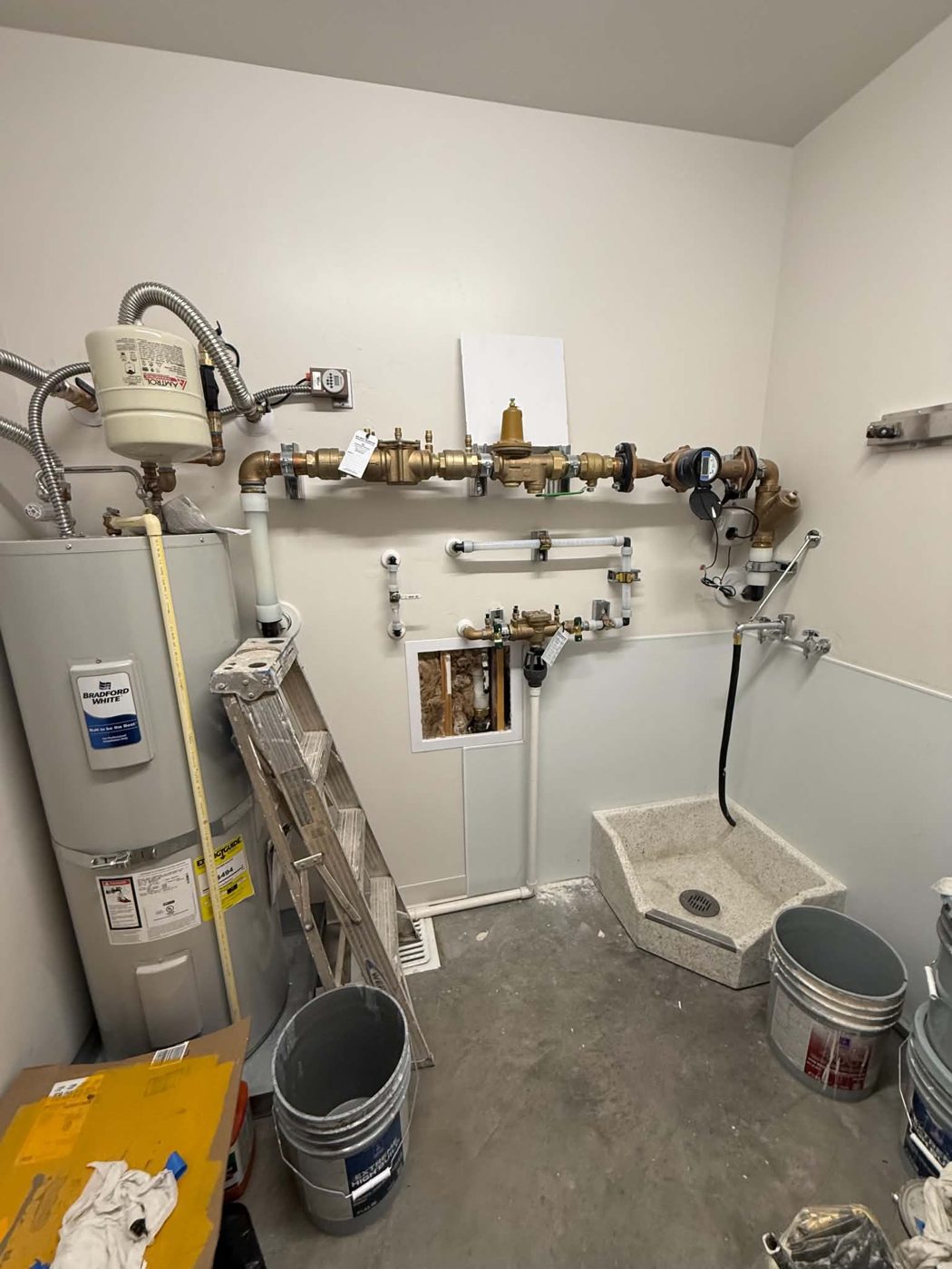 Utility room with water heater, backflow preventer, pressure regulator, and water meter
